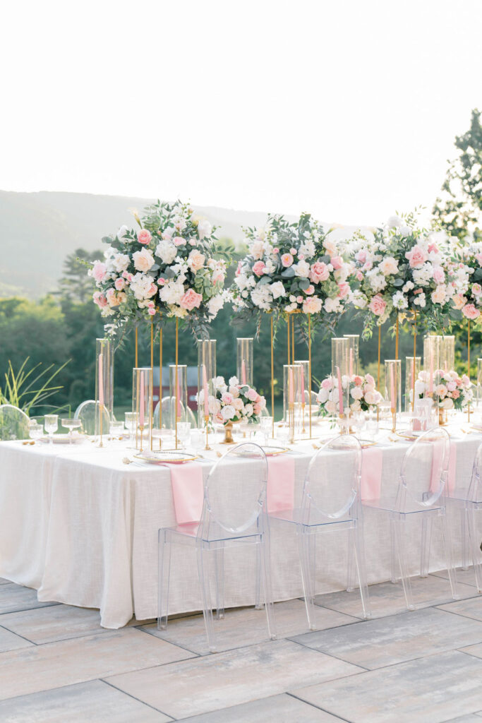 Belle Mer Wedding Price | Caprio Captured Photography Light and Airy Wedding Photography | Elegant outdoor table setting with tall floral centerpieces featuring white and pink flowers. Crystal chairs and soft pink accents create a romantic ambiance.