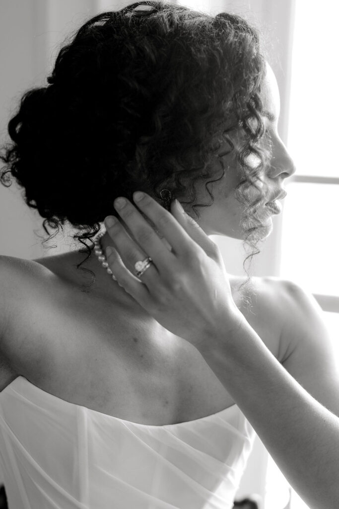 Breakers Mansion Newport Rhode Island | Caprio Captured Photography Light and Airy Wedding Photography | A black and white photo of a woman with curly hair in an elegant updo, wearing a strapless dress and pearl earrings.