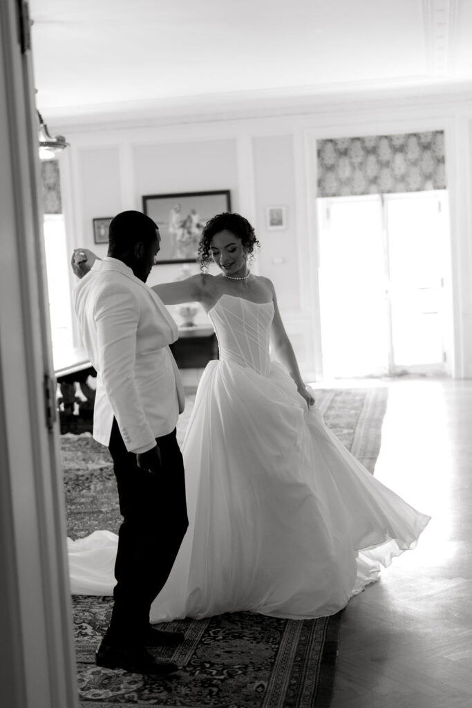 Newport Wedding Photography | Caprio Captured Photography Light and Airy Wedding Photography | Black and white photo of a couple dancing indoors. The woman, in a flowy gown, appears joyful, while the man, in a suit, looks at her warmly.