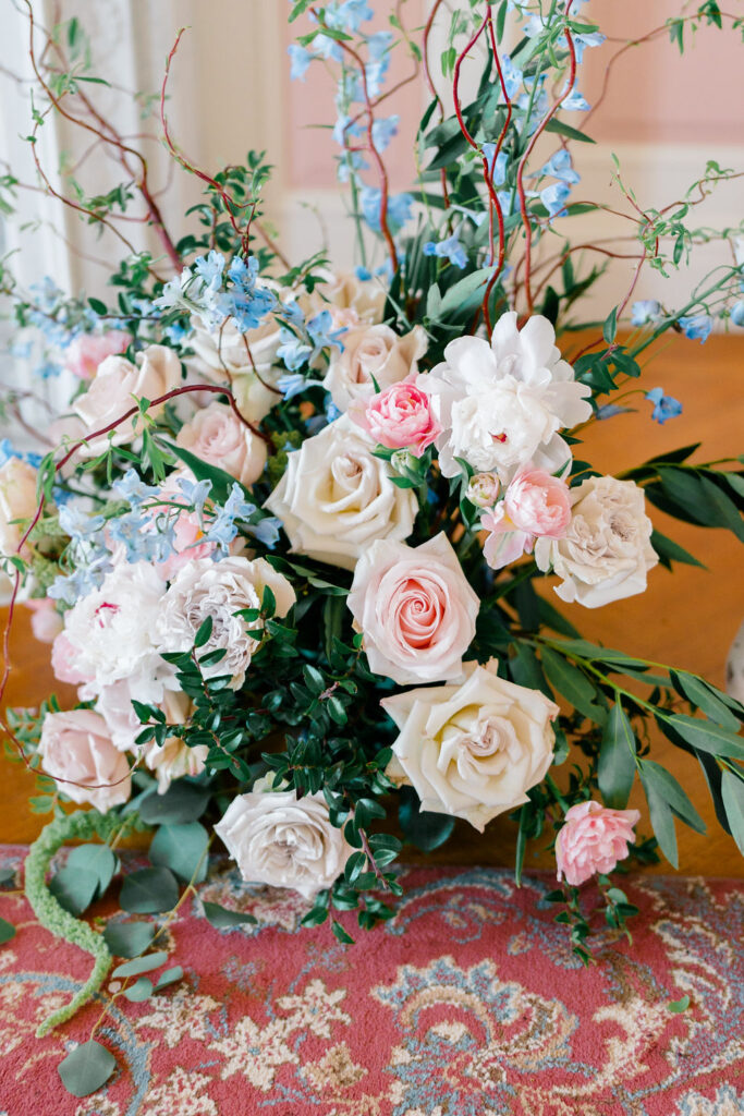 Belle Mer Wedding Price | Caprio Captured Photography Light and Airy Wedding Photography | A vibrant bouquet of pink and white roses, peonies, and blue wildflowers rests on a decorative patterned rug. The arrangement exudes elegance and romance.